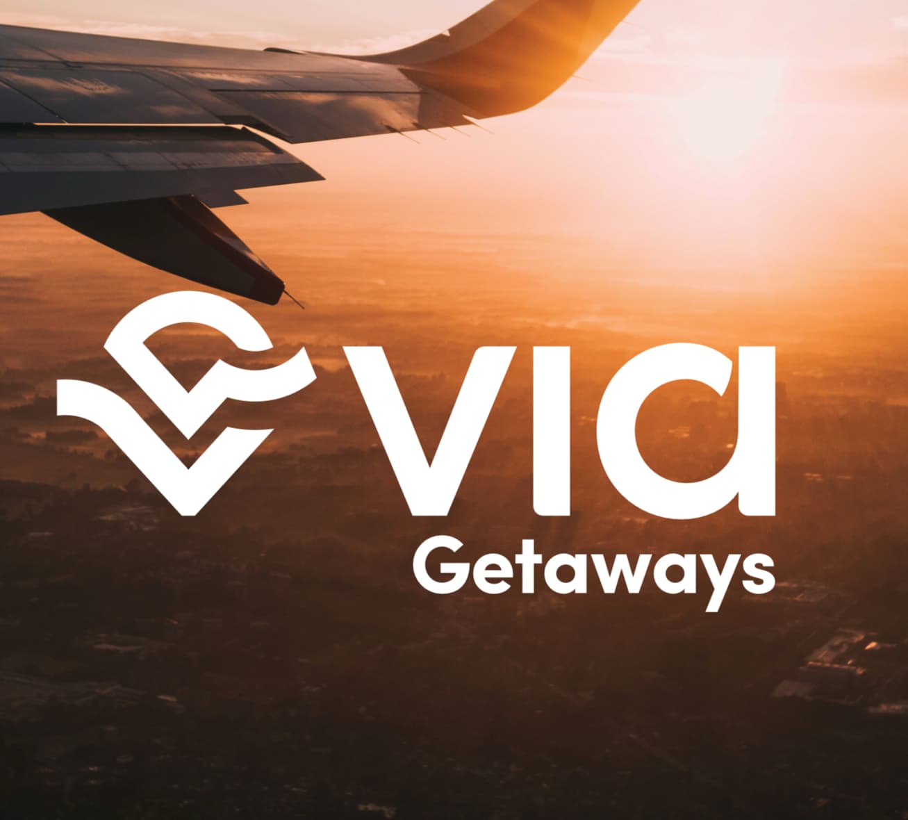 Vista del ala de un avión al atardecer con el logo de Vía Getaways sobrepuesto